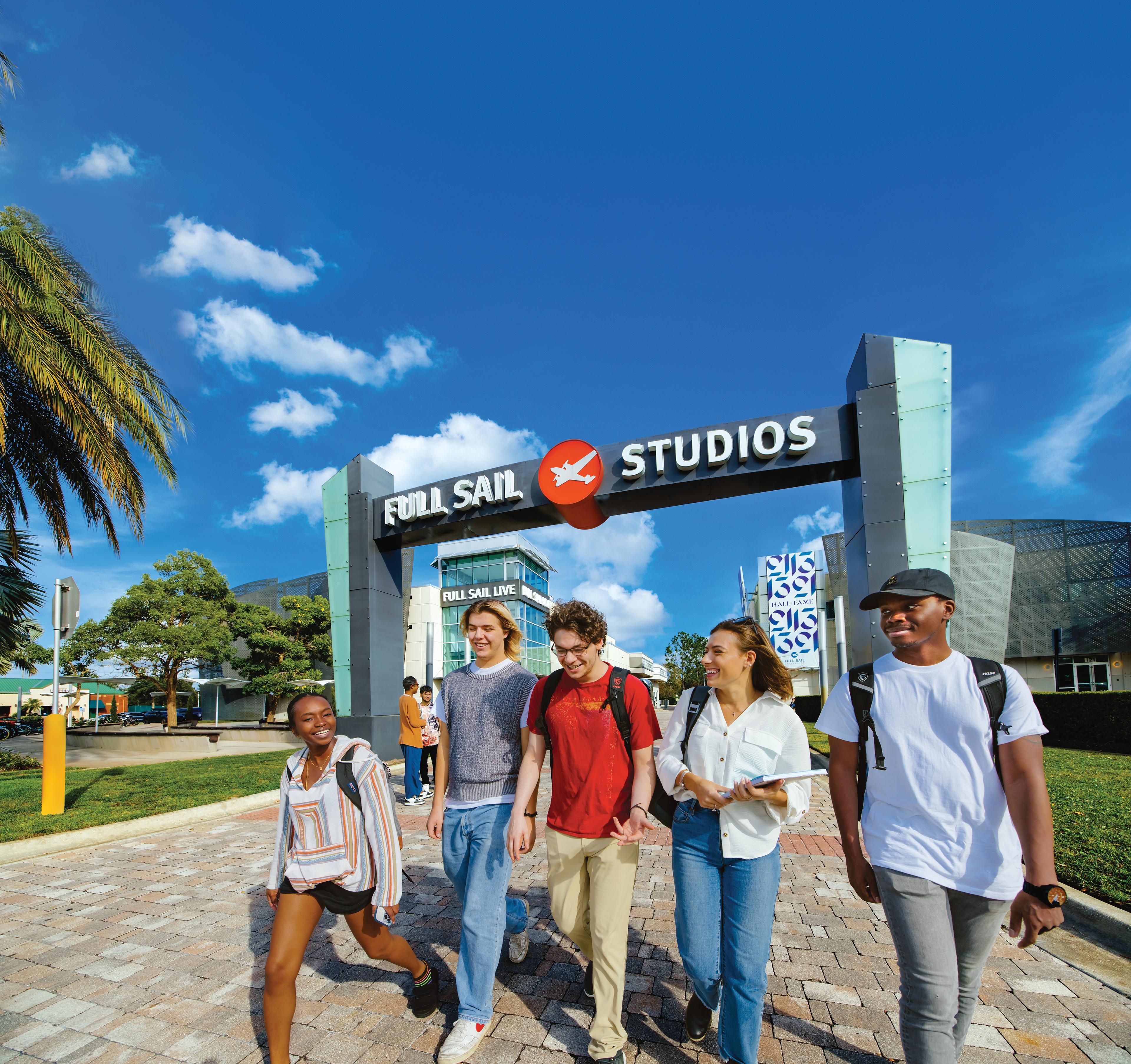 On a bright, sunny campus beneath the Full Sail Studios archway, a group of students with backpacks laugh and walk together.