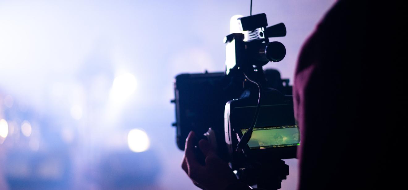 A student holding a piece of professional film equipment views a shot of a scene with ambient lighting.