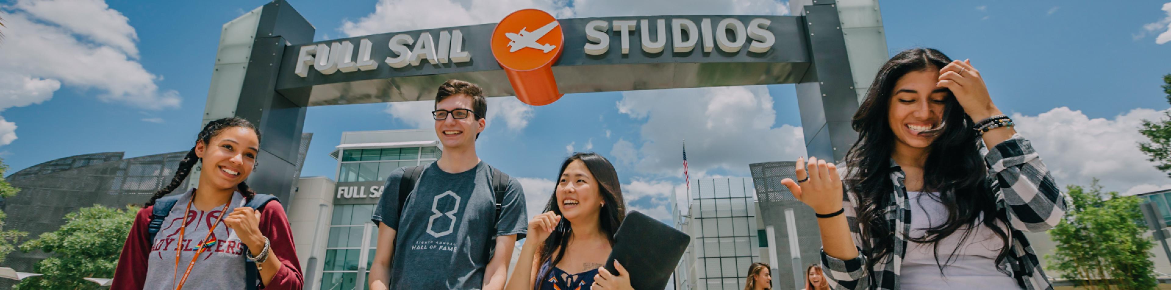 On a bright, sunny campus beneath the Full Sail Studios archway, a group of students with backpacks laugh and walk together.